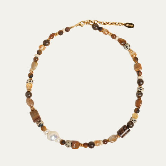 A beaded necklace with a mix of brown, beige, and white beads, including a white pearl and patterned spacer beads, on a light beige background.