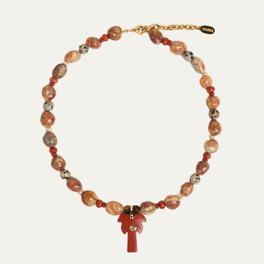 A beaded necklace with irregular terracotta and brown stone beads, small red spacer beads, a gold-tone clasp, and a red palm tree pendant, displayed on a light beige background.