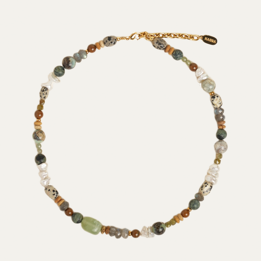 A beaded necklace with a gold chain clasp, featuring a mix of earthy green, brown, white, and black marbled beads, displayed on a light cream background.