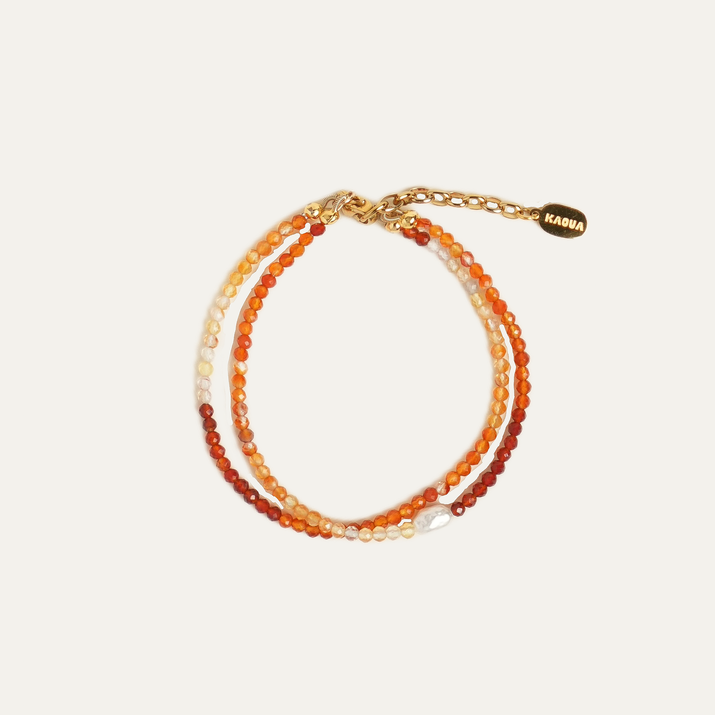 A double-strand beaded bracelet with warm orange, red, and cream beads, featuring a gold-tone chain extender and a small gold brand tag that reads KAOUA.