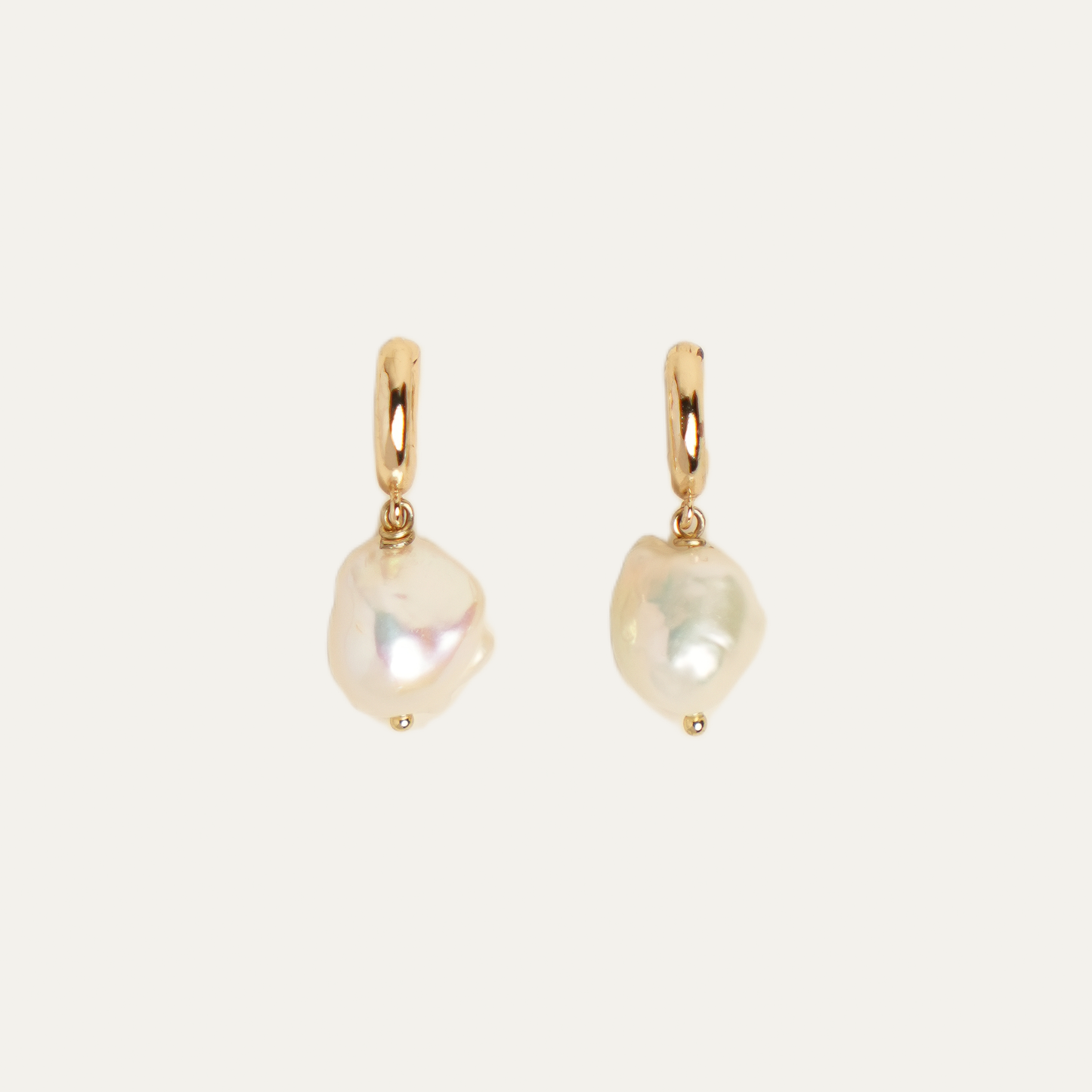 A pair of gold hoop earrings with irregular, baroque-style white freshwater pearls dangling from them, set against a solid off-white background.