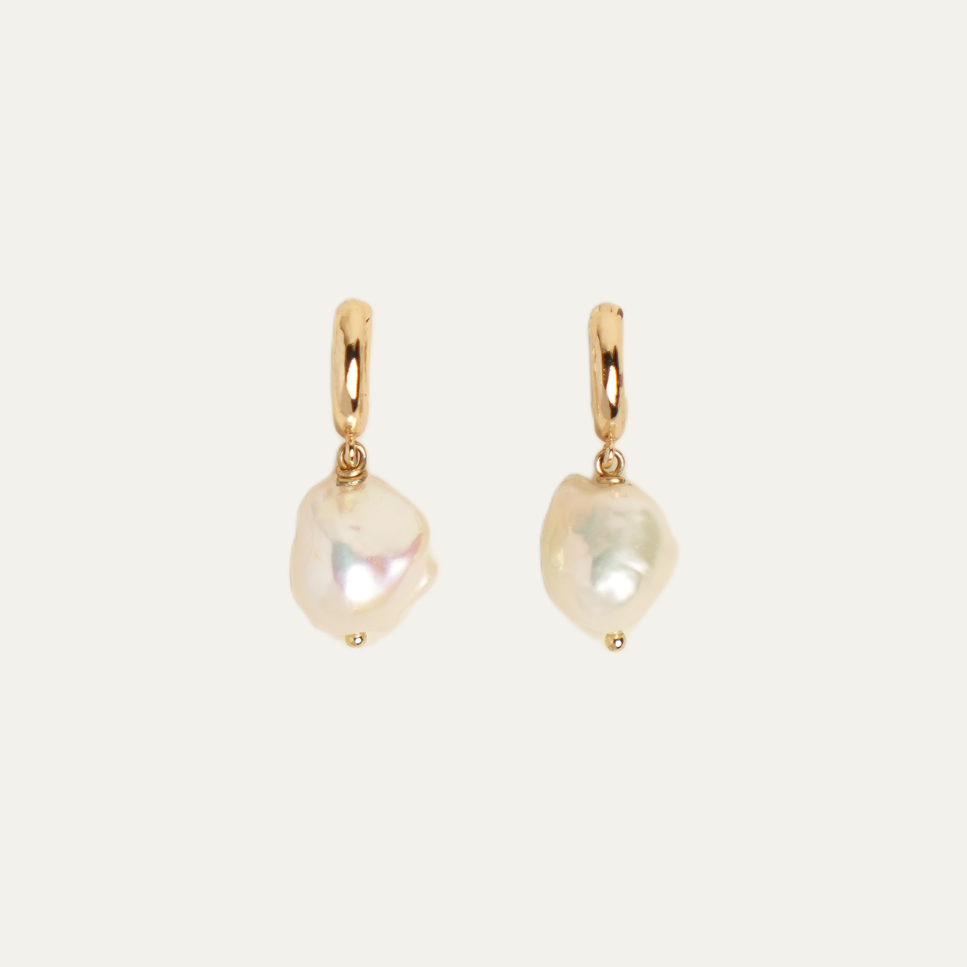 A pair of gold hoop earrings with irregular, baroque-style white freshwater pearls dangling from them, set against a solid off-white background.