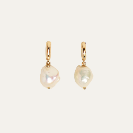 A pair of gold hoop earrings with irregular, baroque-style white freshwater pearls dangling from them, set against a solid off-white background.